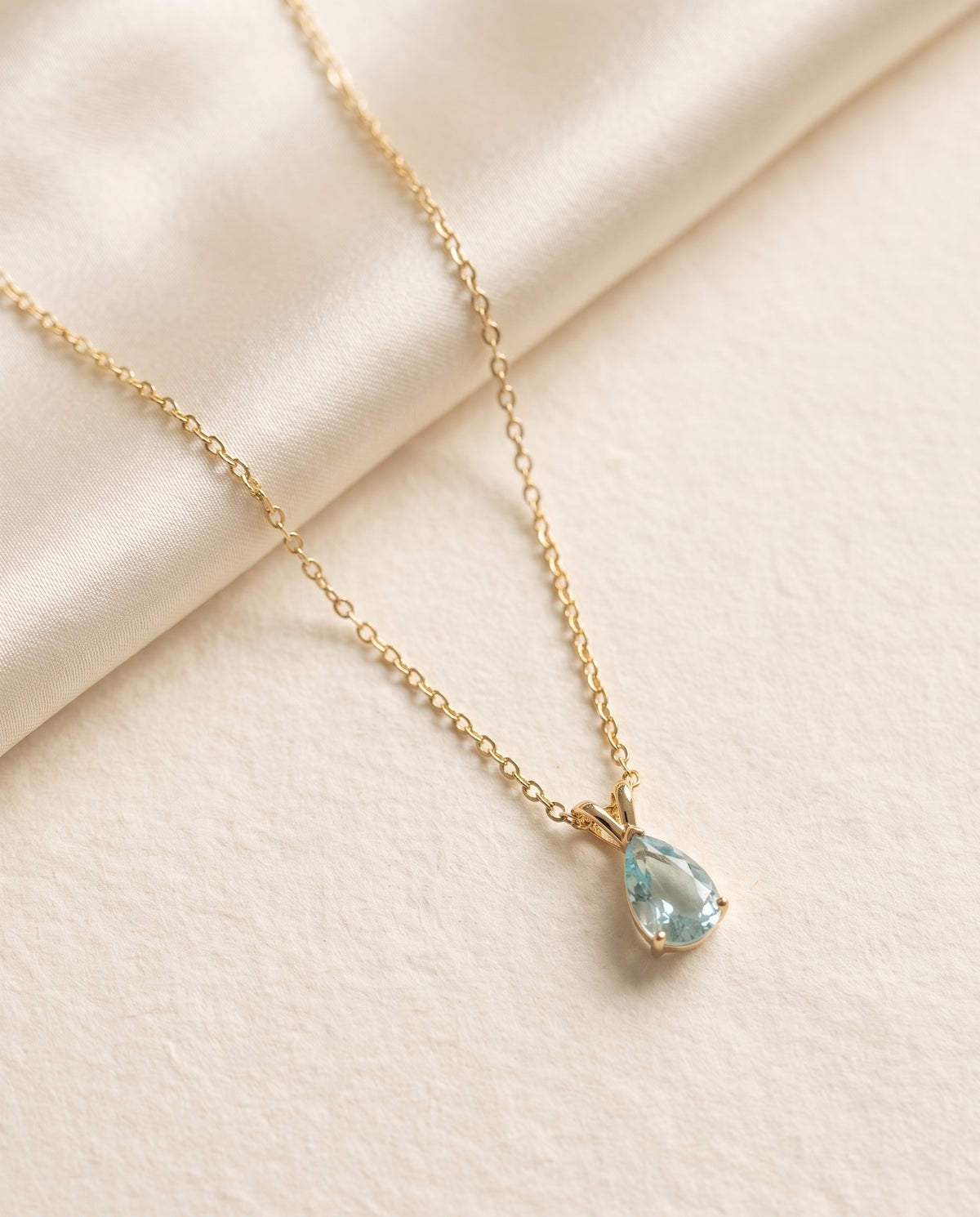 Collier Azur Bellurr posé sur papier crème et satin ivoire