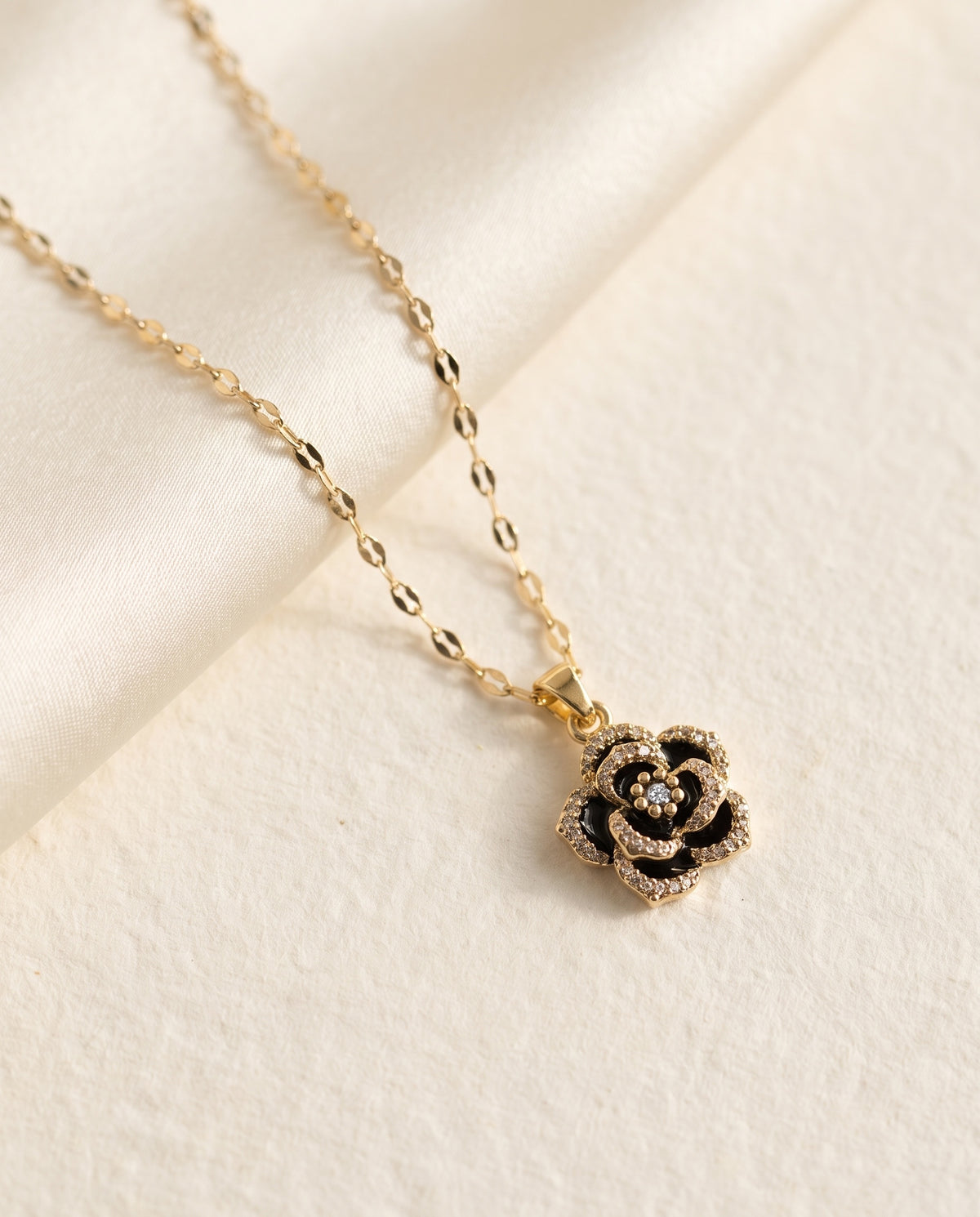 Collier Rose Noire Bellurr posé sur papier crème et satin ivoire